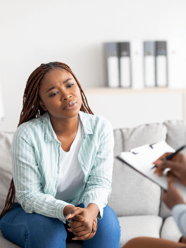 A young black woman thinks with folded hands as her therapist takes notes