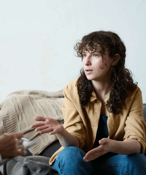 Curly-haired brunette woman sitting on a couch, expressing herself to a therapist