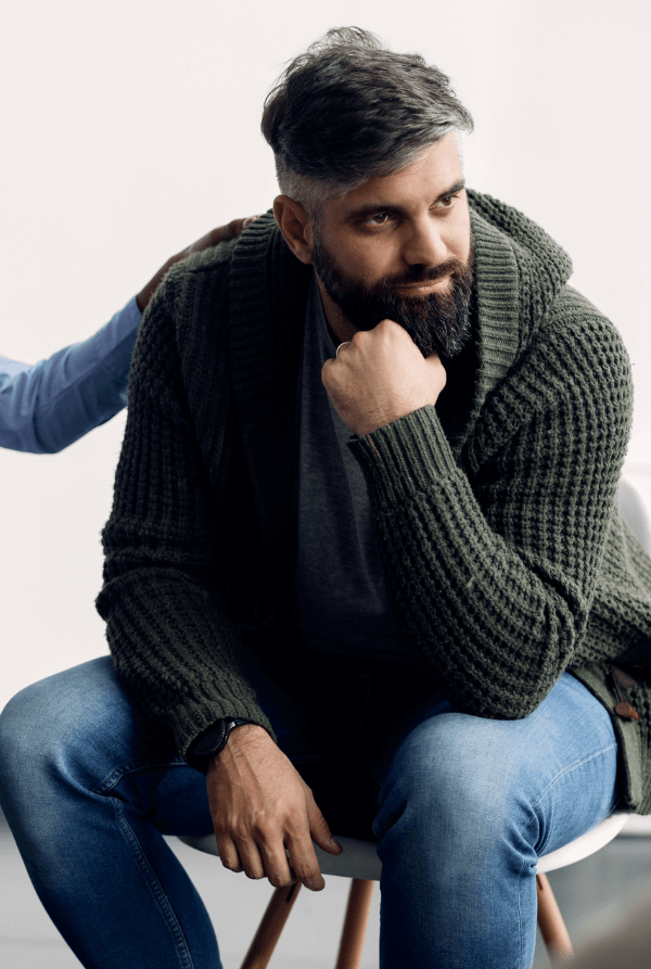 A man thinks and looks into the distance while a therapist has her hand on his shoulder in group therapy