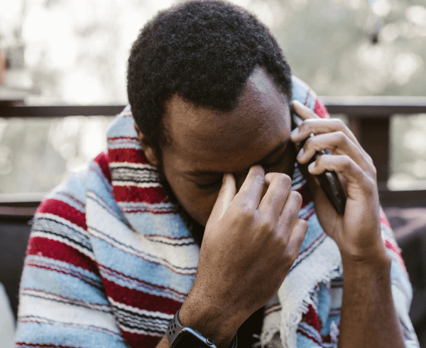 Black man on the phone with his other hand near his nose bridge
