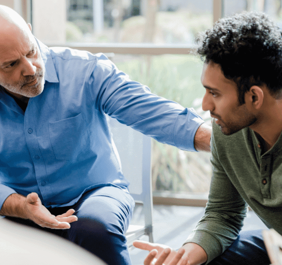 Senior man with his hand on the shoulder of a younger man during a short-term addiction treatment therapy session