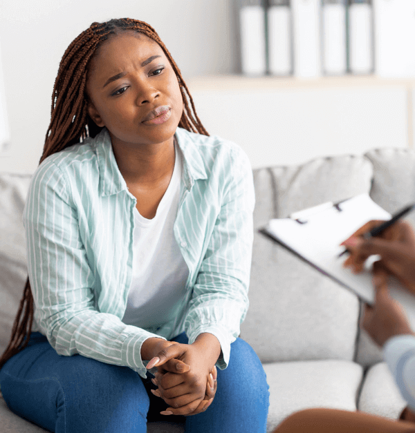 Young black woman with braids sitting quietly as a therapist takes notes