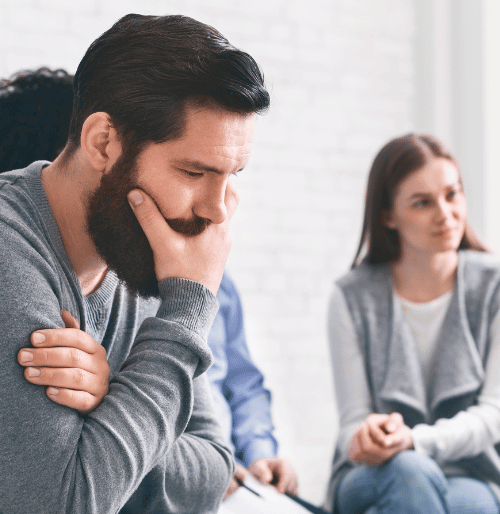 Man thinking with one hand over his mouth during addiction rehab group therapy